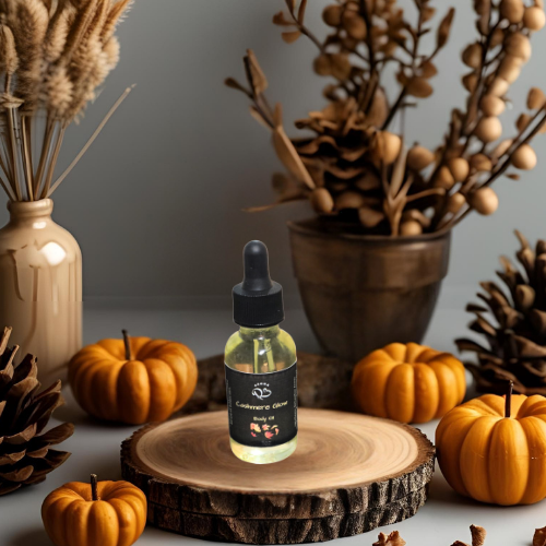 Bottle of 'Cafeteria Gourmet' body oil on a wooden coaster with pumpkins and decorative plants.