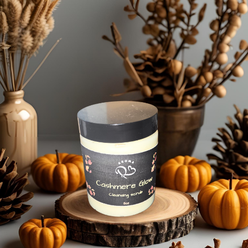 Candle labeled 'Cashmere Glow' on a wooden coaster with pumpkins and decorative branches in the background.